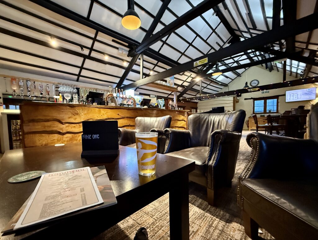 Interior of the Stable Bar at Stowford Farm Meadows with leather armchairs, wooden bar, tables and high beamed ceiling.