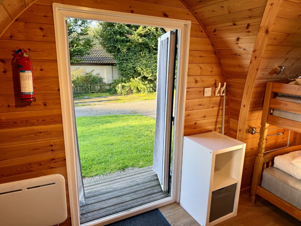 Interior of a wooden camping pod at Stowford Farm Meadows with bunk beds, electric heater, storage unit and doors opening onto the grass