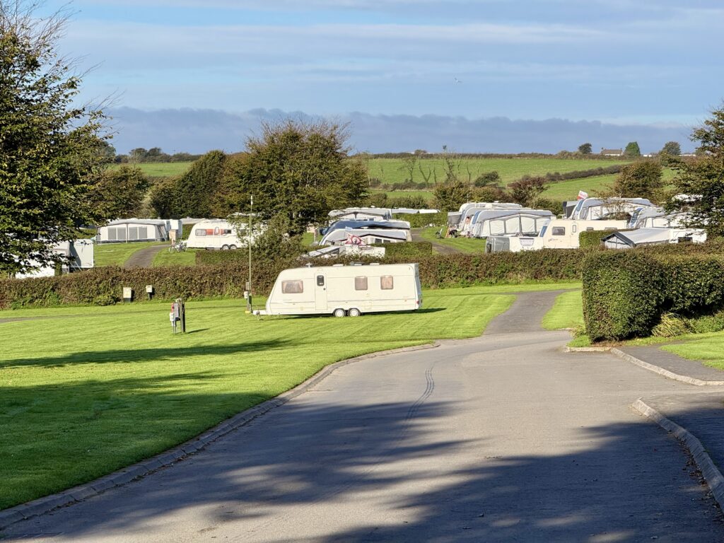 Touring caravans on spacious grass pitches divided by hedges at Stowford Farm Meadows, surrounded by rolling North Devon countryside.