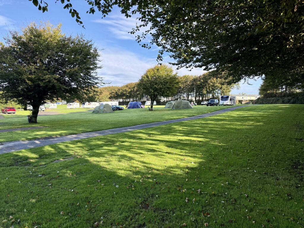 Tents, caravans and motorhomes on spacious grass camping pitches surrounded by trees at Stowford Farm Meadows