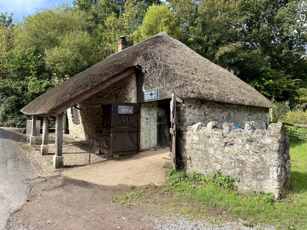 Historic thatched Branscombe Forge with stone walls and its open wooden doors, surrounded by trees in Branscombe, Devon.