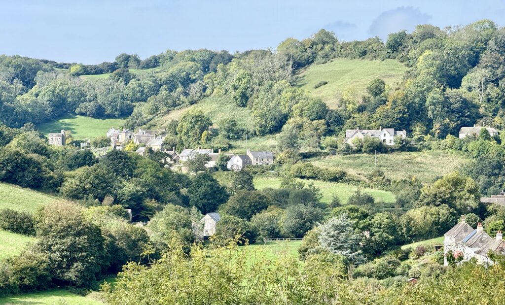 Branscombe village spread through a lush green East Devon valley, with St Winifred’s Church, cottages, fields and wooded hillsides.