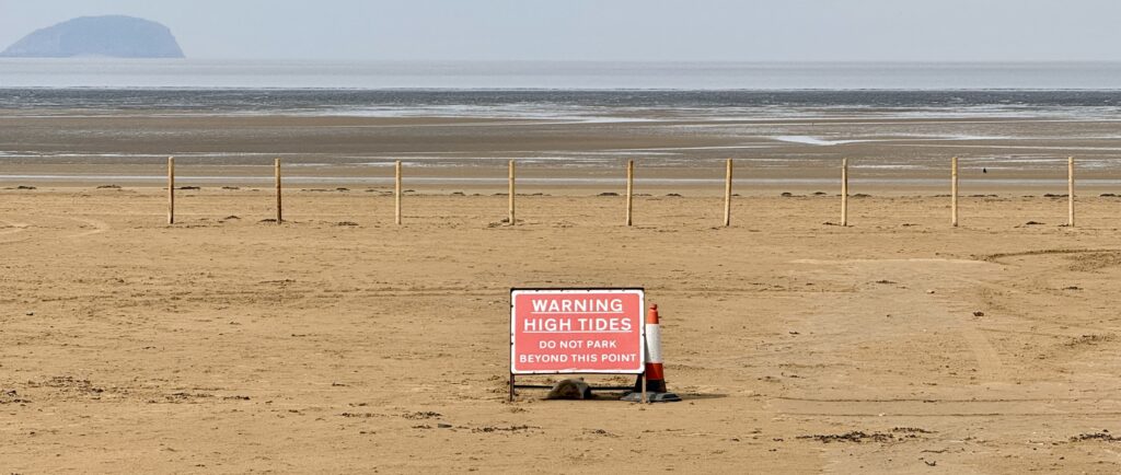 Weston-super-Mare tides at low water with high tide warning sign and Steep Holm beyond.