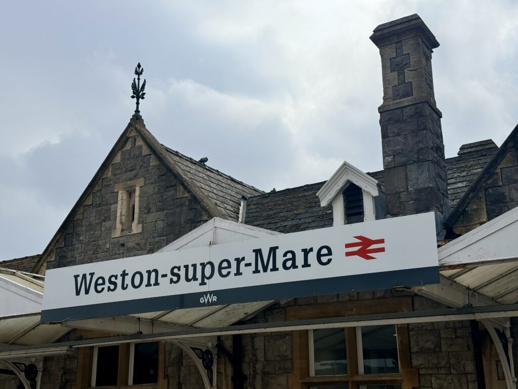 Weston-super-Mare railway station sign on the platform beneath the historic stone station building.