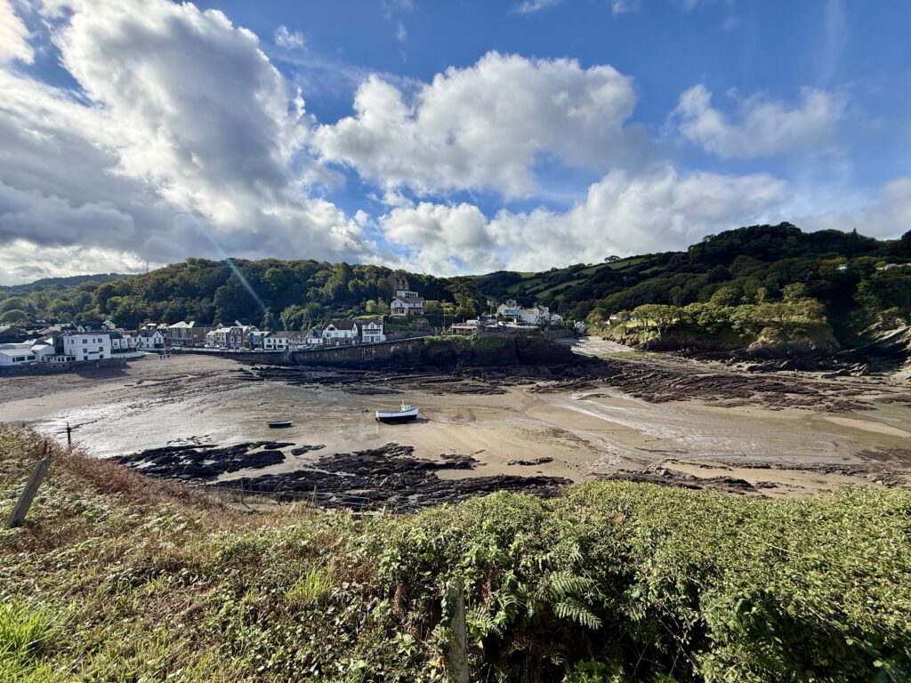 Combe Martin beach and village at low tide with fishing boats, rocky shoreline and wooded North Devon hills.