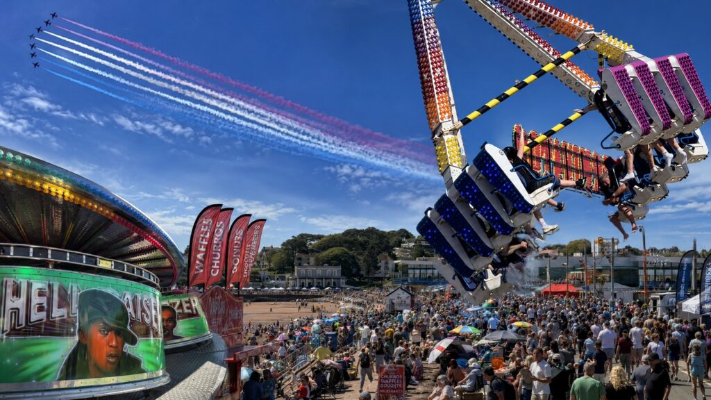 Red Arrows trailing red, white and blue smoke above crowds and fairground rides on Paignton seafront during the Torbay Airshow in Devon. Credit: ThisIsSouthWest
