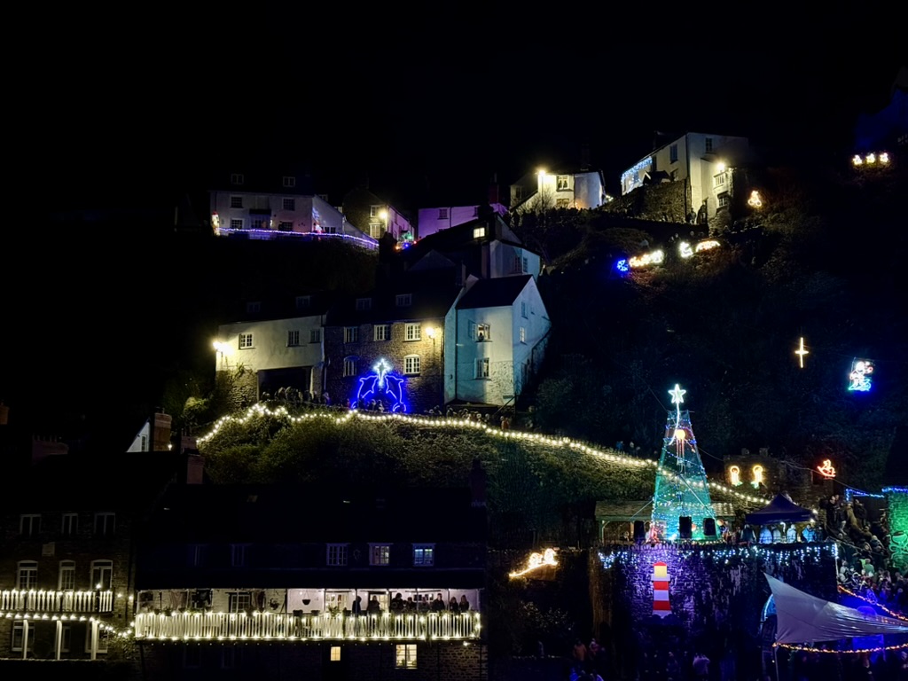 Clovelly's hillside cottages and harbour illuminated with colourful Christmas lights after dark.