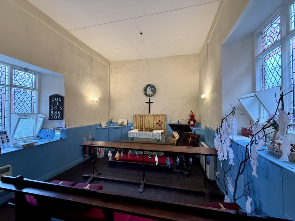 Interior of St Peter's Chapel in Clovelly with wooden pews, altar and stained-glass windows.