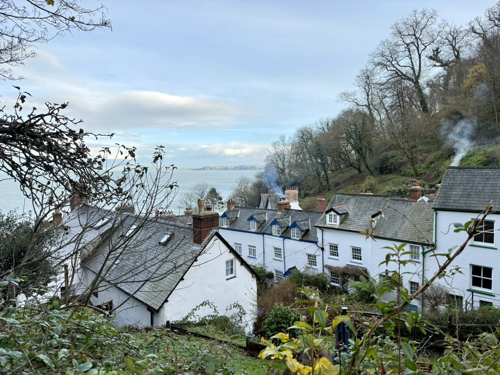 **Alt text:** White cottages with slate roofs descending Clovelly's wooded hillside towards the sea on the North Devon coast.