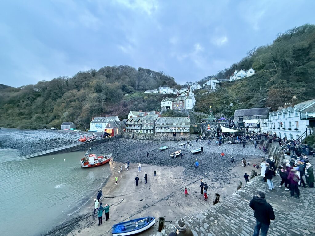 Clovelly harbour at low tide with visitors on the beach, fishing boats and white cottages climbing the wooded hillside.