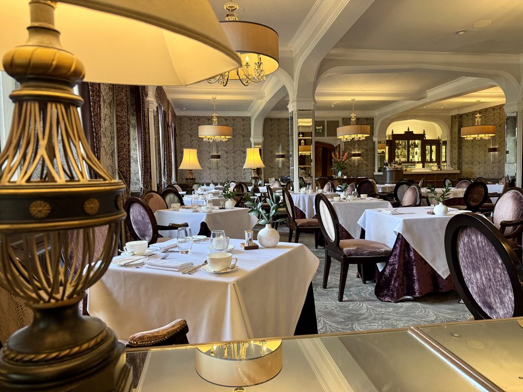 Great Western Grill restaurant at Bovey Castle, with white tablecloths, elegant dining tables, chandeliers and traditional furnishings.