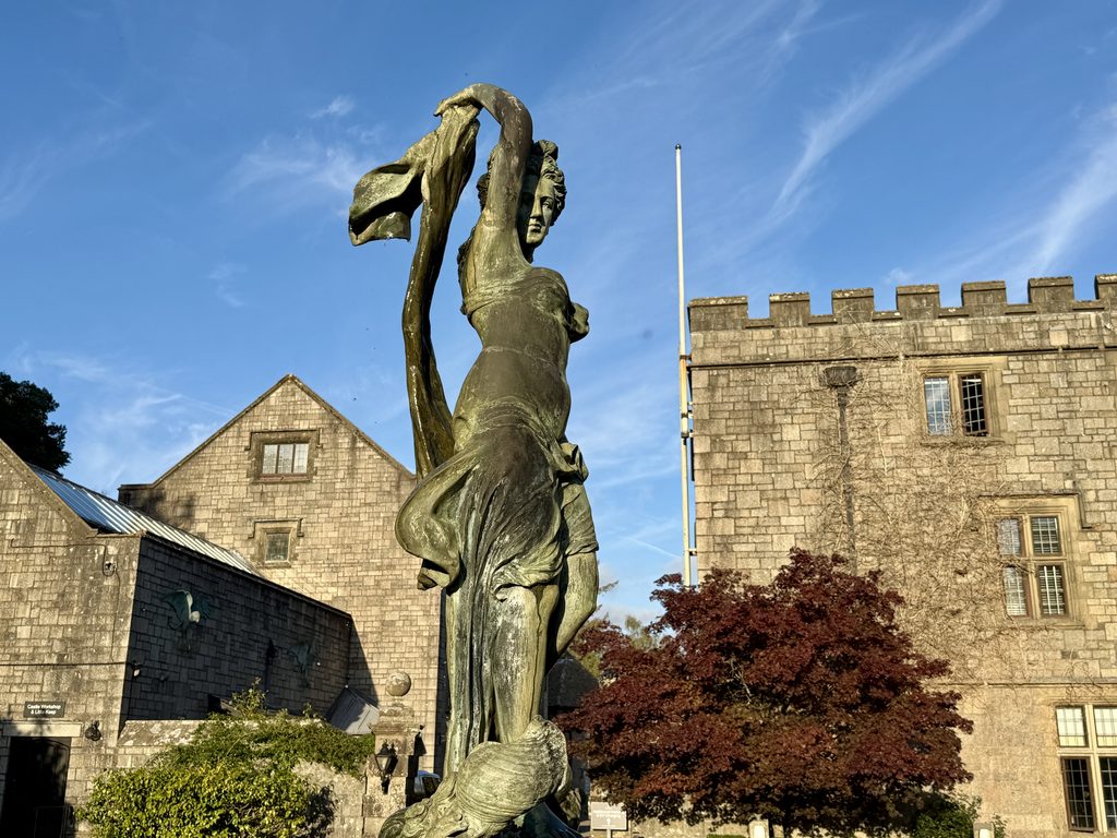 Bronze statue of a woman standing in front of Bovey Castle’s stone buildings, seen on arrival at the Dartmoor hotel in Devon.