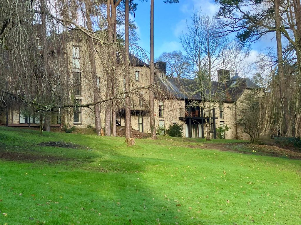 Stone holiday lodges at Bovey Castle surrounded by woodland and lawns within the Dartmoor estate.