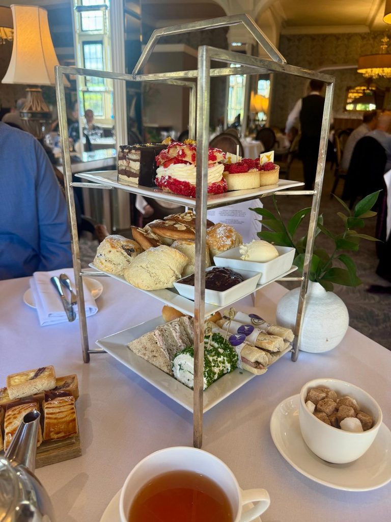 Three-tier afternoon tea stand at Bovey Castle with finger sandwiches, savouries, scones with jam and cream, cakes and pastries, with a cup of tea in the foreground.
